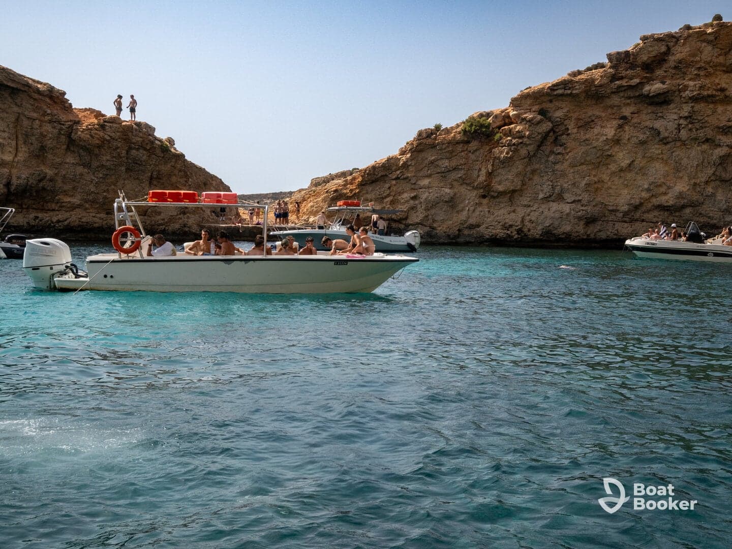 A lively group enjoys a day on the water, surrounded by stunning cliffs and clear turquoise waters — perfect for swimming and exploring.
