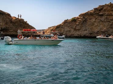 A lively group enjoys a day on the water, surrounded by stunning cliffs and clear turquoise waters — perfect for swimming and exploring.