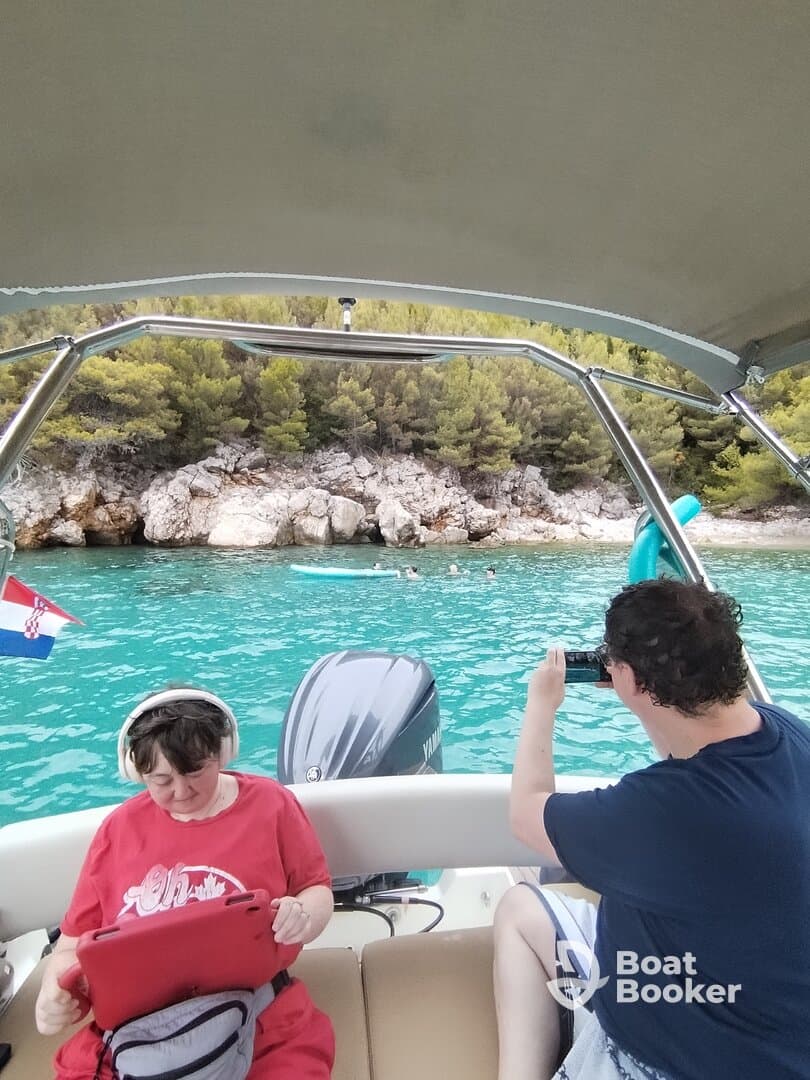 Guests enjoy a day on the water, capturing memories while relaxing on a boat with a scenic backdrop of rocky shores and clear turquoise waters.