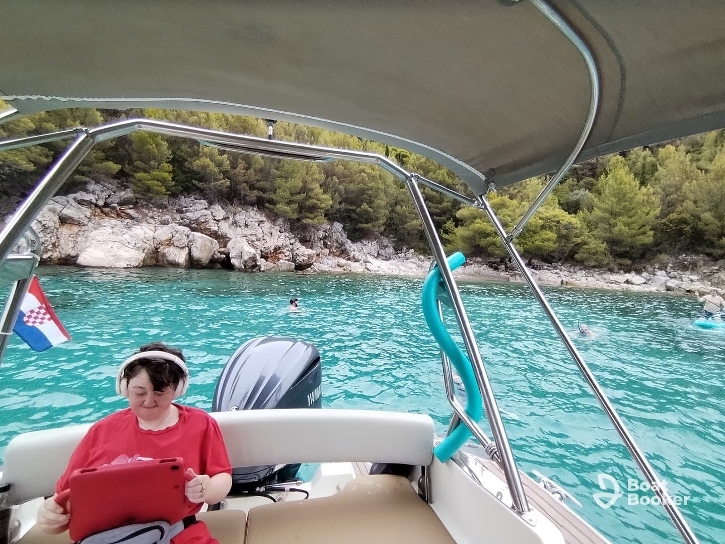 A guest enjoys some leisure time on a boat in Croatia, using a tablet while others swim in the clear turquoise waters — a perfect day for relaxation and fun on the water.