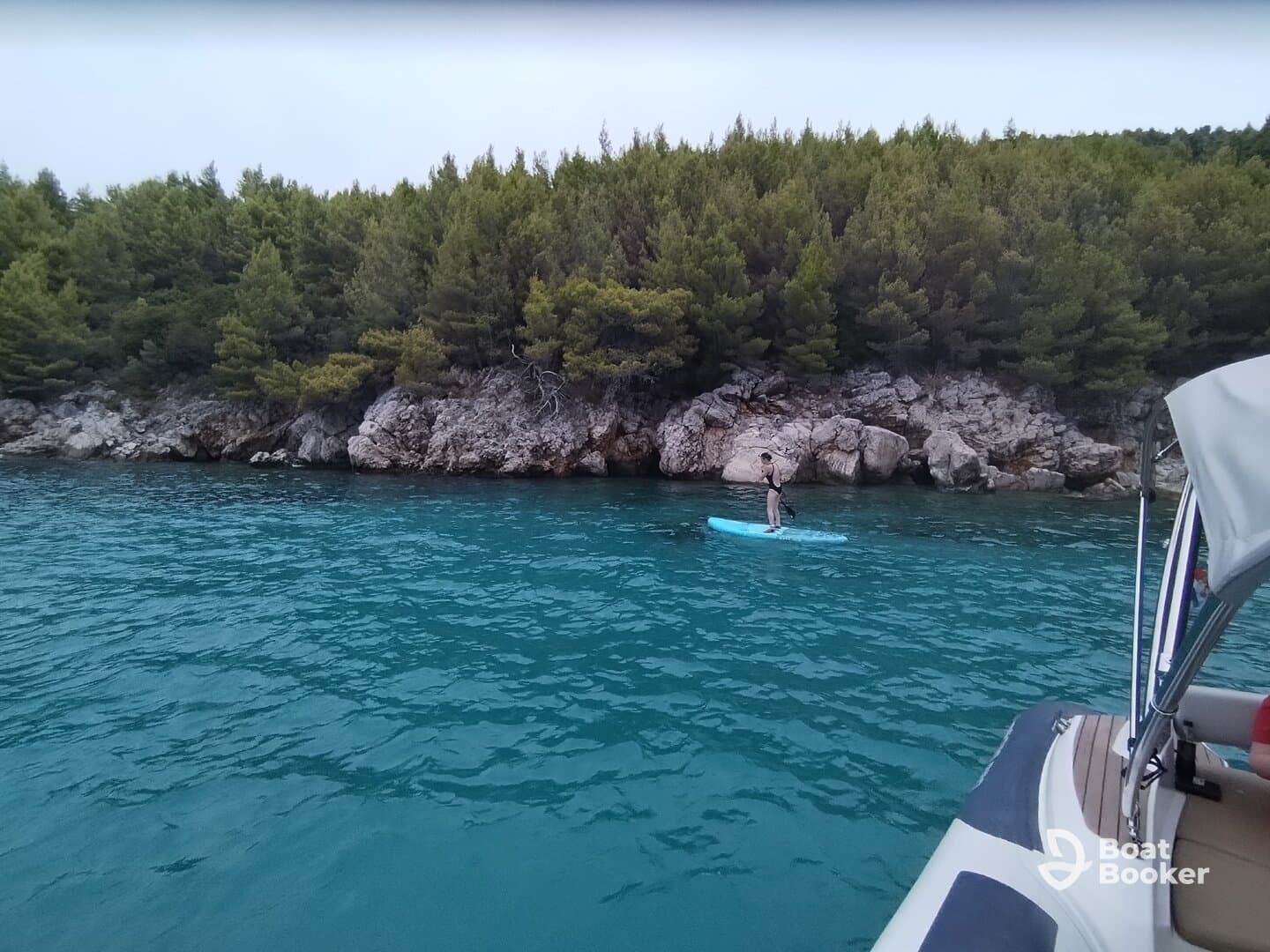 A paddleboarder glides across the turquoise waters near a rocky shoreline, showcasing the serene beauty of the coastal landscape.