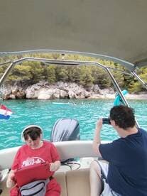 Guests enjoy a day on the water, capturing memories while relaxing on a boat with a scenic backdrop of rocky shores and clear turquoise waters.