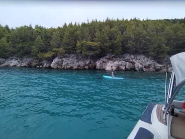 A paddleboarder glides across the turquoise waters near a rocky shoreline, showcasing the serene beauty of the coastal landscape.