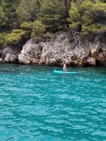 A person paddleboards in crystal-clear waters near a rocky shoreline, showcasing the beauty of outdoor water activities in a serene setting.