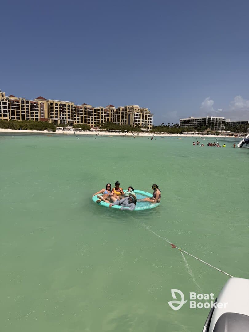 A lively group enjoys a fun day on a floating mat in the clear waters, surrounded by a beautiful beach backdrop — perfect for summer adventures.