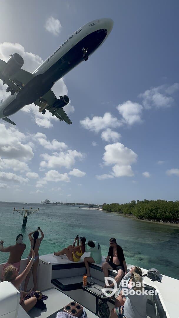 A lively group aboard a boat captures the moment as an airplane flies overhead, creating a unique backdrop for their fun day on the water.