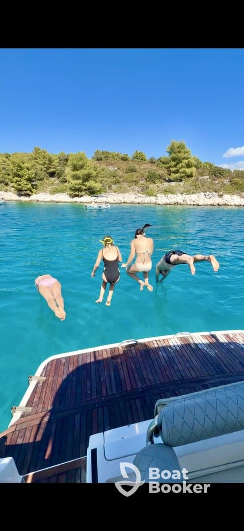 A group of friends joyfully jumps into the crystal-clear waters from a boat, capturing the essence of summer fun and adventure on the water.