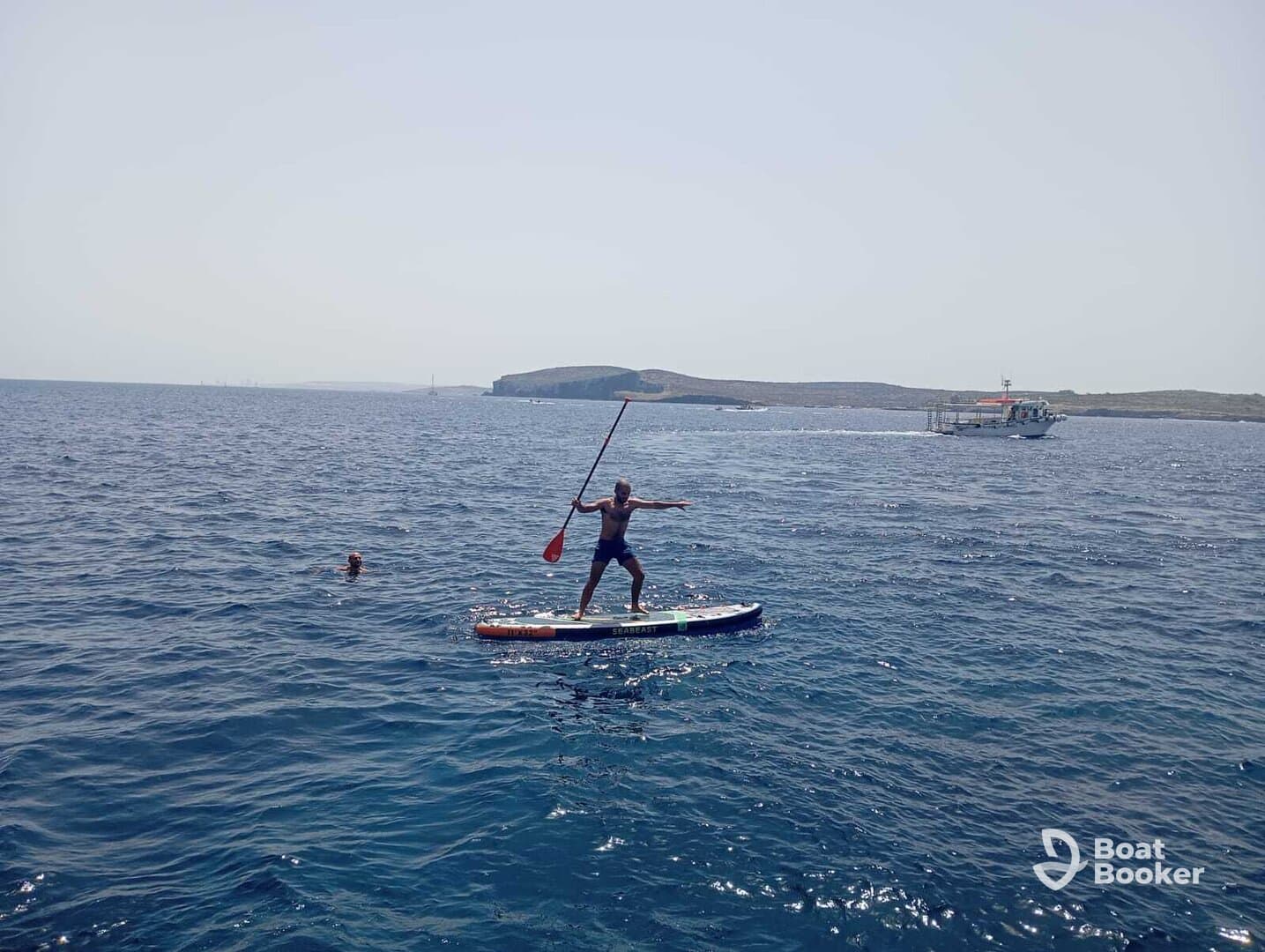 A thrilling moment of paddleboarding on clear waters, with a swimmer nearby, showcasing the excitement of on-water activities.