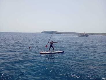 A thrilling moment of paddleboarding on clear waters, with a swimmer nearby, showcasing the excitement of on-water activities.