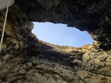 An unclear view from inside a cave looking up towards the sky, showcasing rocky formations. The image lacks identifiable subjects or clarity.