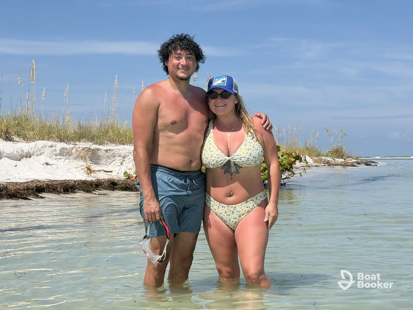 A couple enjoys a sunny day at the beach, wading in shallow waters, perfect for snorkeling and relaxation.