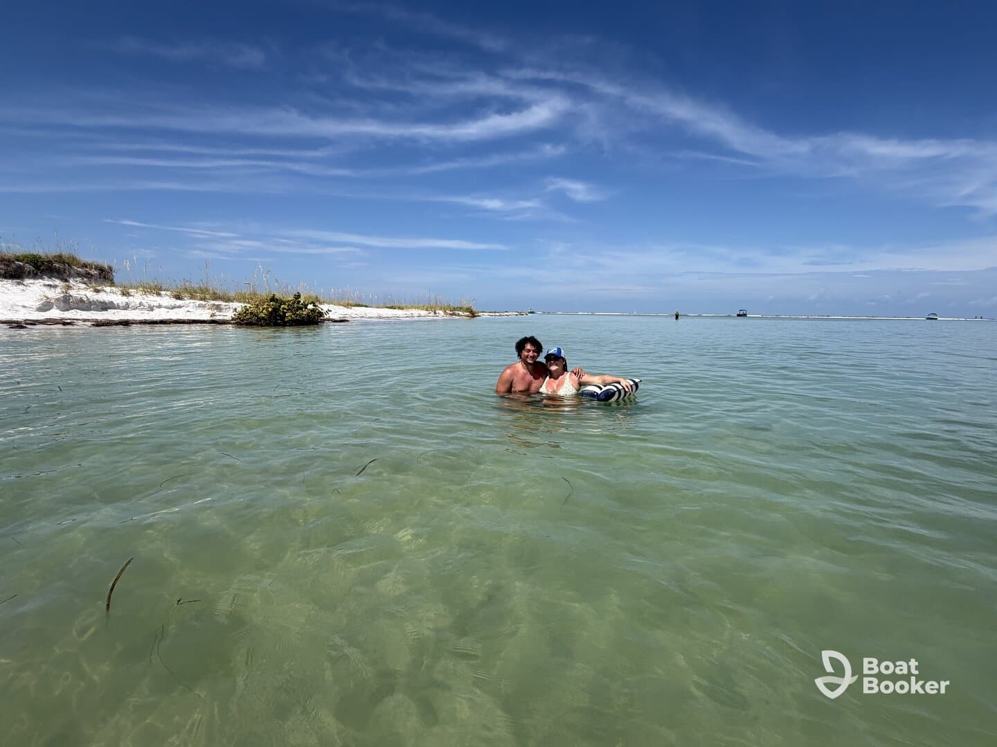 A couple enjoys a refreshing swim in shallow waters at a picturesque sandbar, surrounded by beautiful scenery — perfect for a fun day on the water.