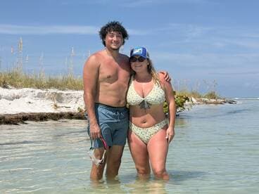 A couple enjoys a sunny day at the beach, wading in shallow waters, perfect for snorkeling and relaxation.