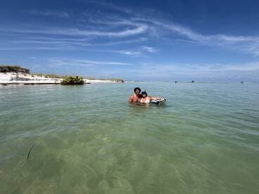 A couple enjoys a refreshing swim in shallow waters at a picturesque sandbar, surrounded by beautiful scenery — perfect for a fun day on the water.