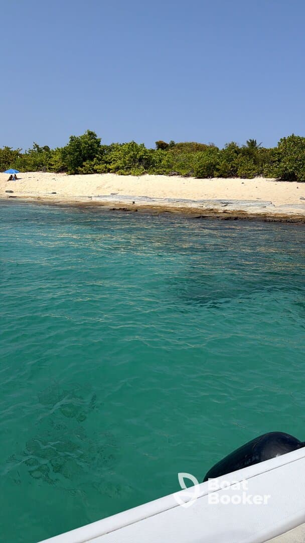 A serene view of a beach with a person relaxing under an umbrella, showcasing the beautiful turquoise waters and lush greenery — perfect for a tranquil getaway.