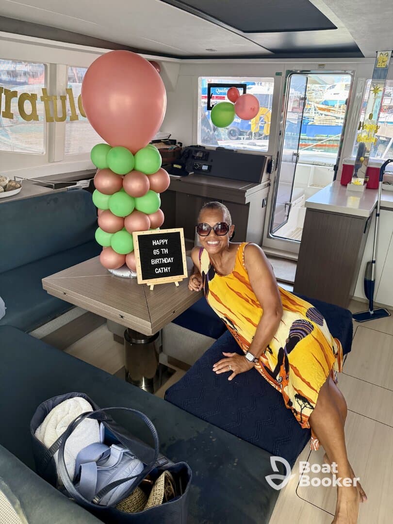 A woman celebrates her 65th birthday inside a beautifully decorated boat cabin, complete with balloons and a festive sign — perfect for memorable celebrations on the water.