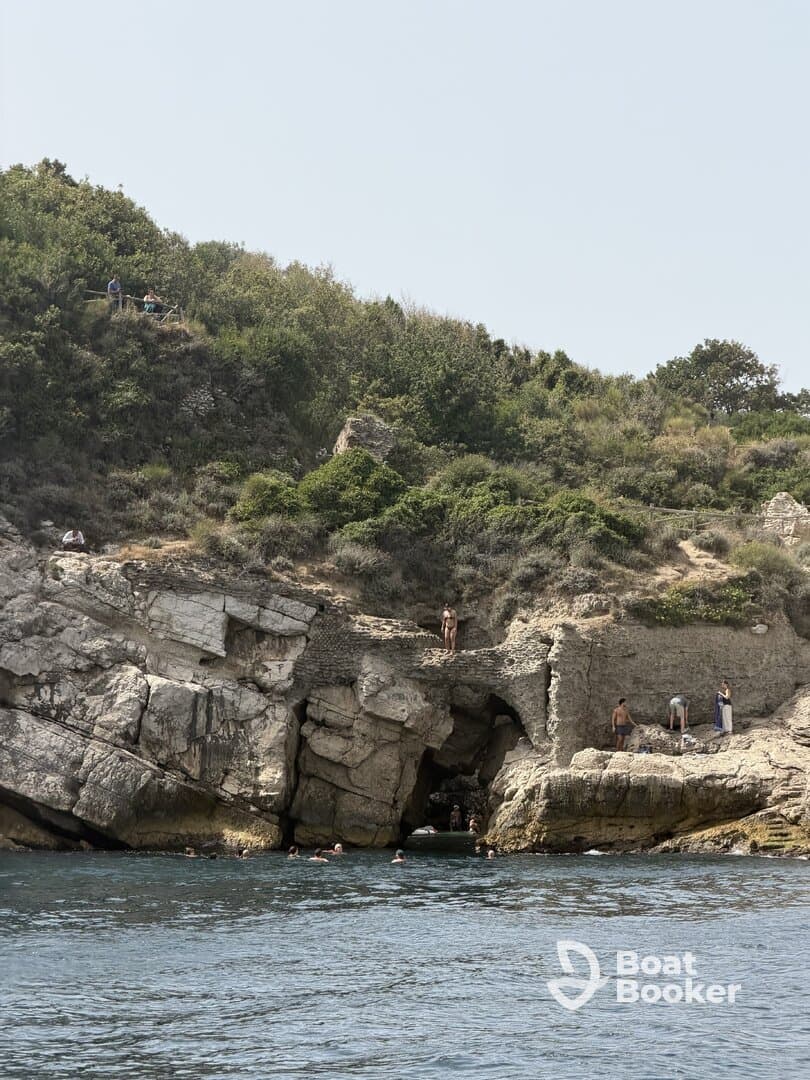 A lively scene of swimmers enjoying the clear waters near a rocky coast, with people exploring the shoreline — a perfect summer getaway.