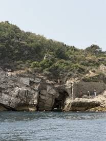 A lively scene of swimmers enjoying the clear waters near a rocky coast, with people exploring the shoreline — a perfect summer getaway.
