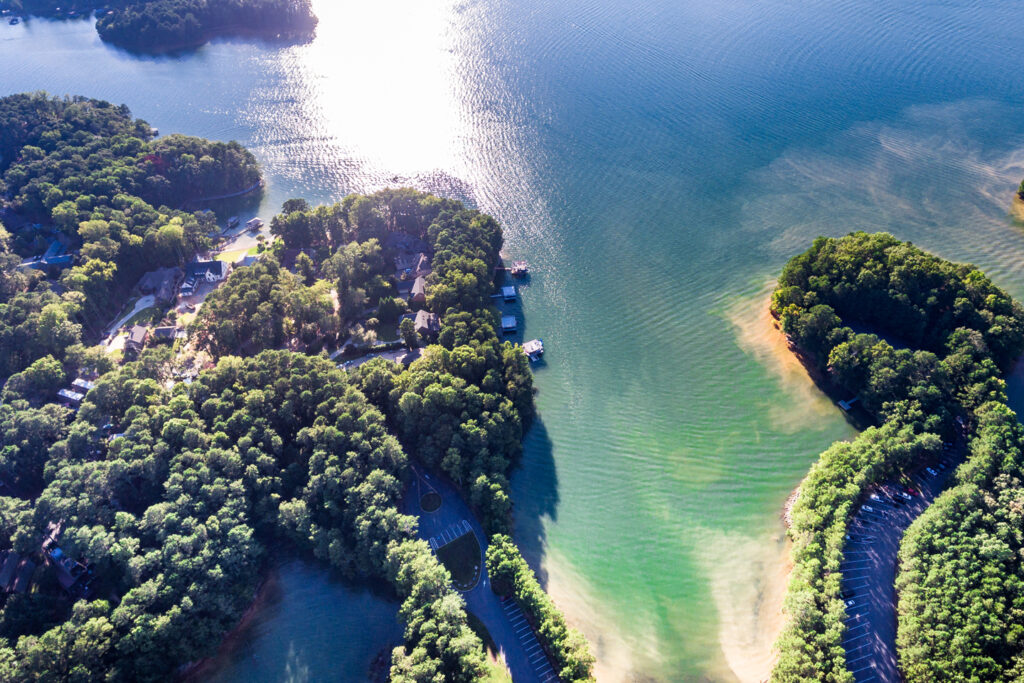 A bird's eye view of a bay in Lake Lanier with greenery and crystal clear waters visible on a sunny day.