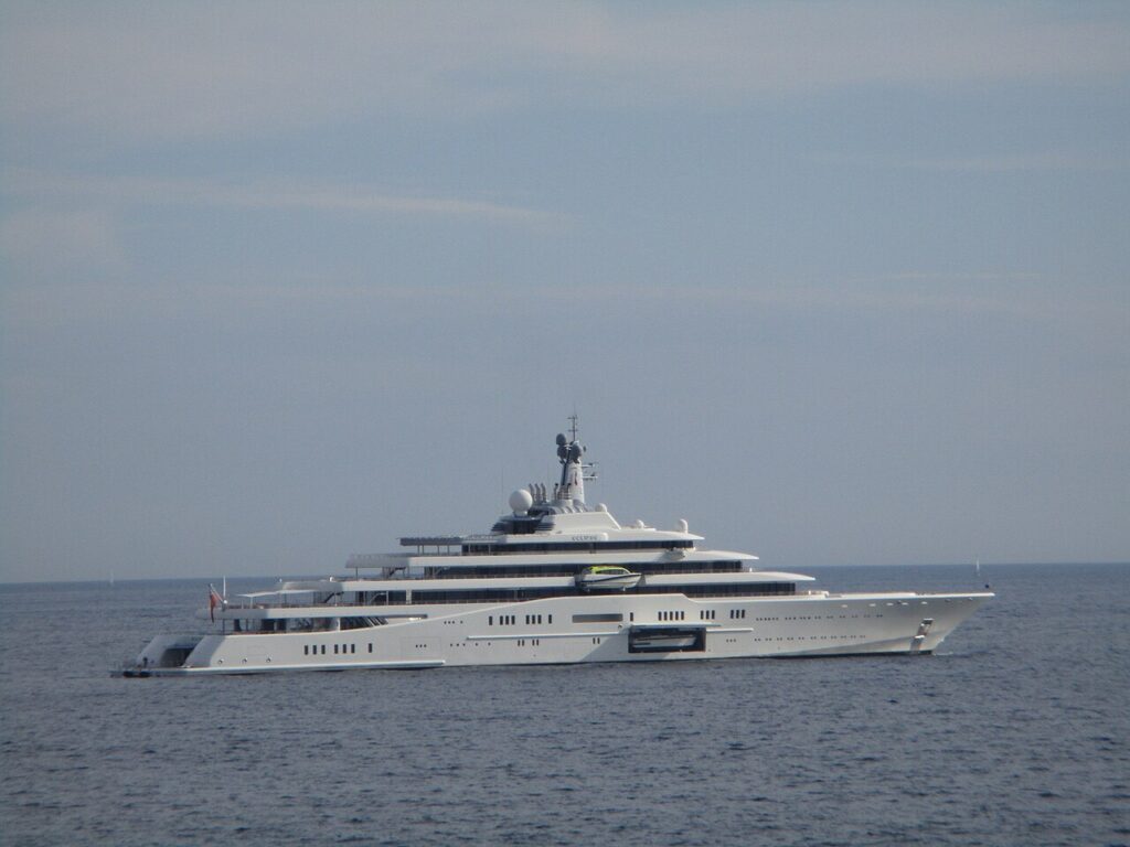 A large white luxury yacht's anchored on calm blue water under a partly cloudy sky.