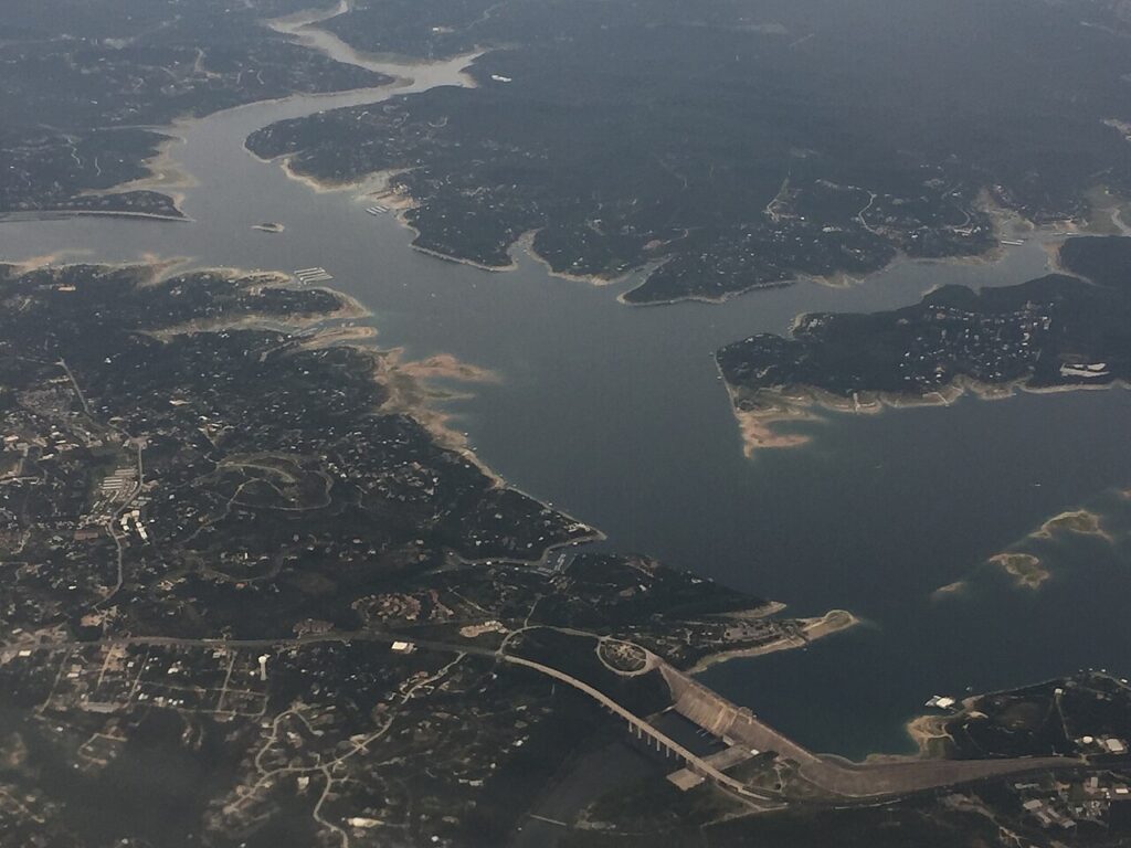 Here's an aerial view of a large lake—one of the best for boating—with a winding shoreline, surrounding hills, scattered buildings, and a dam at the bottom.