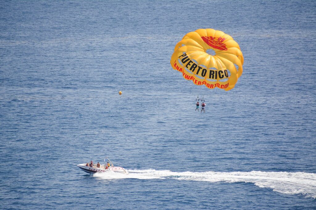 A yellow parasail with "Puerto Rico" on it pulls two people above the ocean, towed by a motorboat with three people onboard.